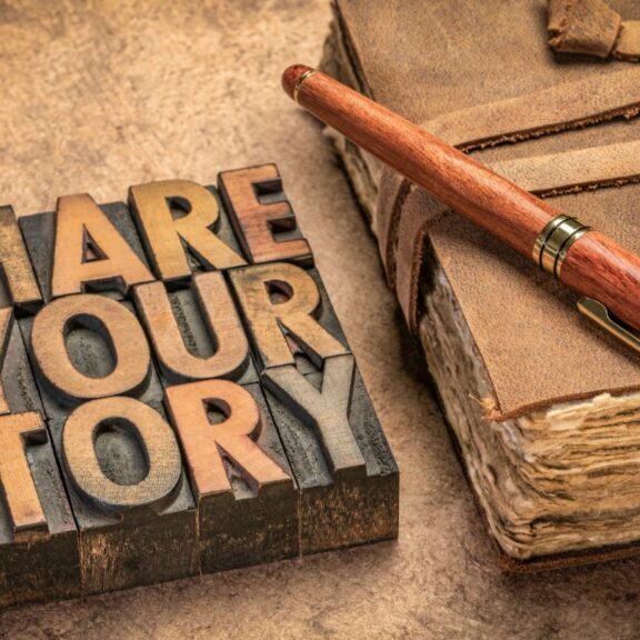 Everybody has one. A story that is. My story is not yours and yours is not mine.  The details vary - except for one thing. God is the Author! NOtebook and a sign on a table that reads "Share Your Story"